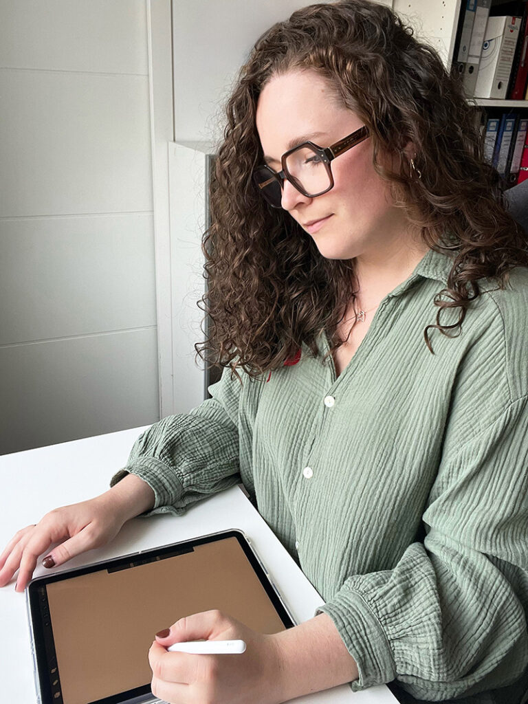 Portrait professionnel de la graphiste indépendante travaillant pour Nekae Studio, en train de travailler sur la création de supports de communication sur sa tablette graphique.