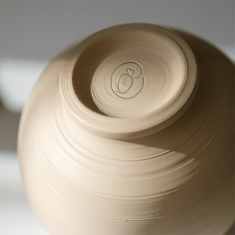 Logo céramique artisanale de Voyage terrestre incrusté sous une poterie, par Nekae Studio.