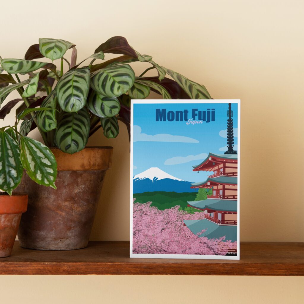 Petite affiche illustrée du Mont Fuji au Japon posée sur une étagère en bois, avec une plante en arrière-plan